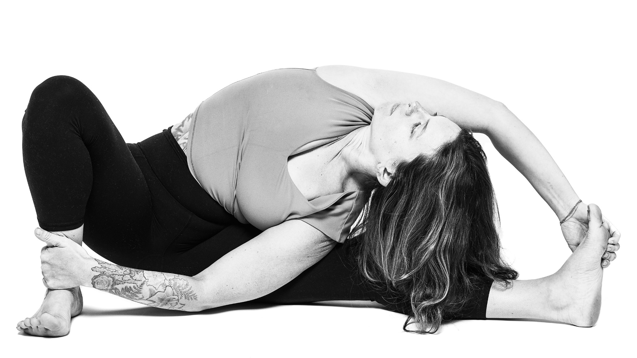 A yoga teacher in a reclining side stretch on a white seamless background.