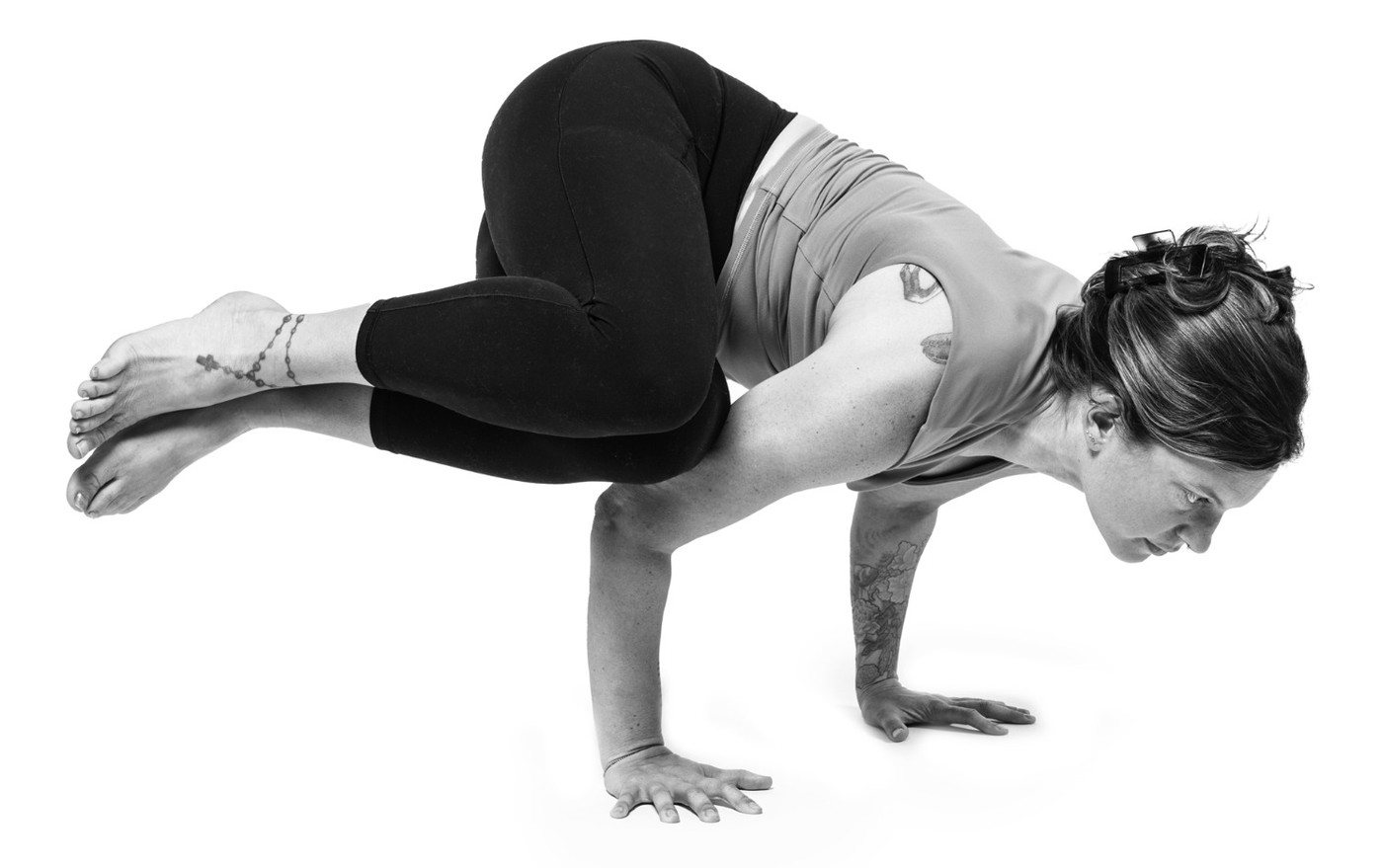 A yoga teacher balancing in crow pose on a white seamless background.