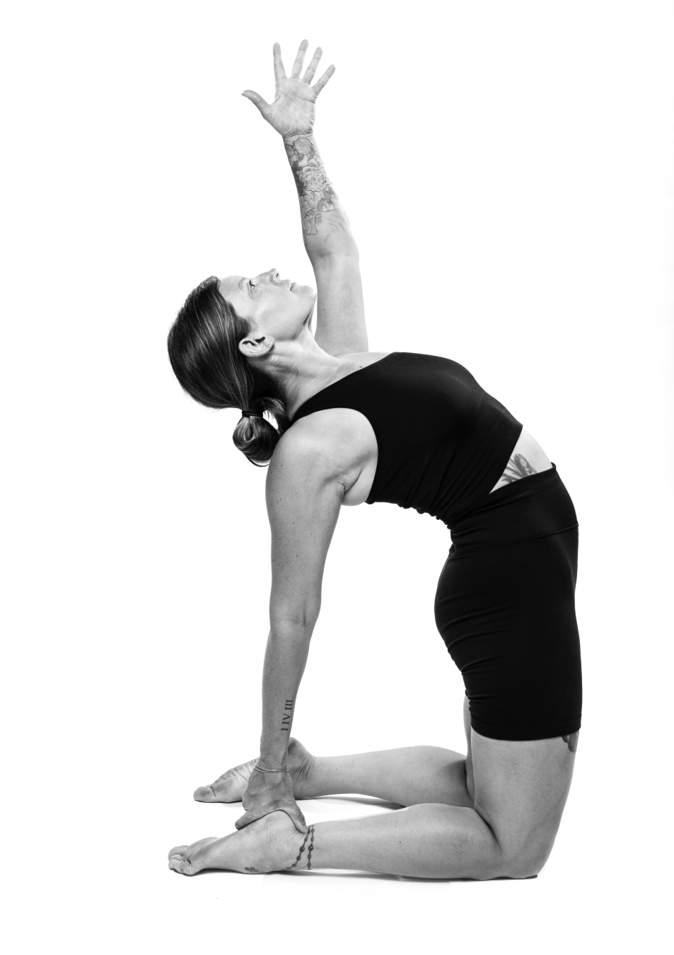 A full-length black-and-white yoga portrait made against a white seamless background.
